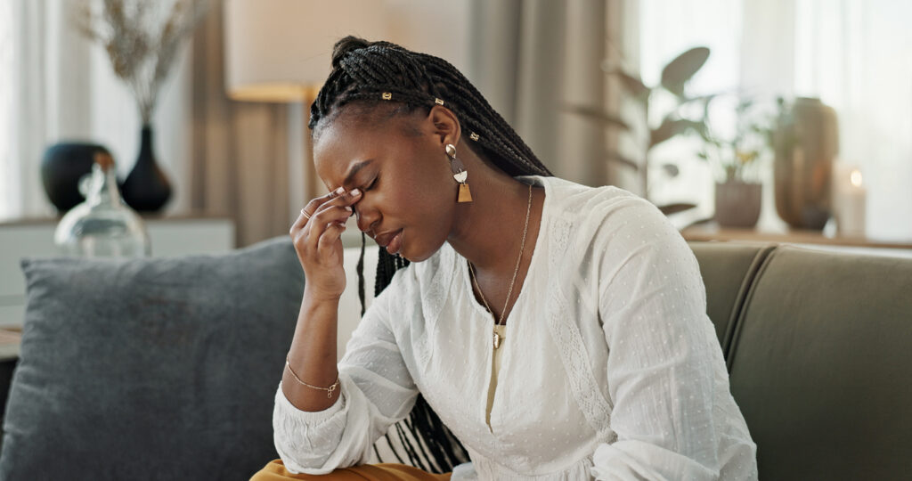 young woman looking stressed sat on her sofa.