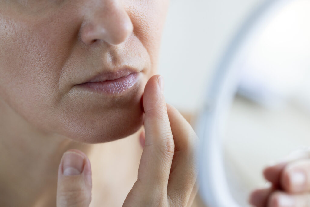 closeup of a woman examining her facial skin in a mirror.
